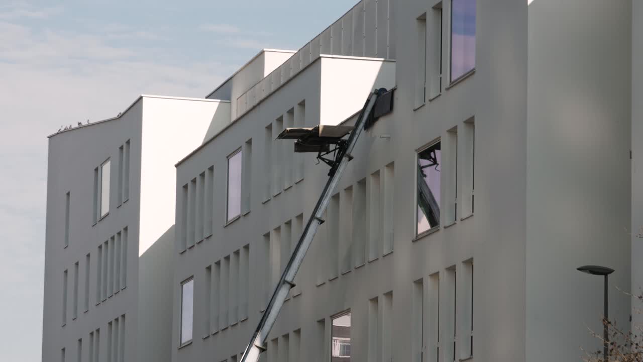 A moving platform lift ascends the facade of a white apartment building, used for transporting furniture to upper floors