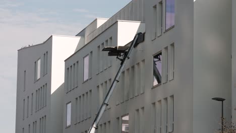 a moving platform lift ascends the facade of a white apartment building, used for transporting furniture to upper floors