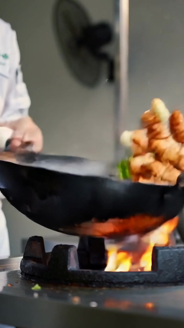 Video verticale: Chef che salta il cibo in giacca bianca in un wok nero su un fornello acceso per rosolare.