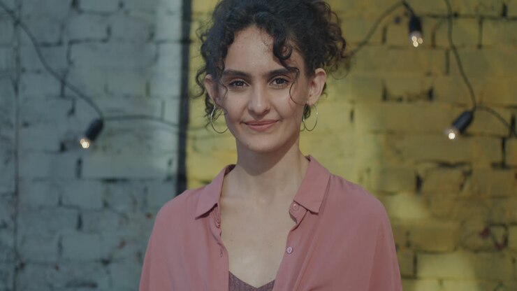 Donna sorridente davanti a un muro di mattoni con lucine