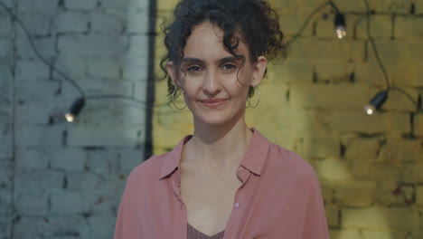 smiling woman in front of brick wall with string lights