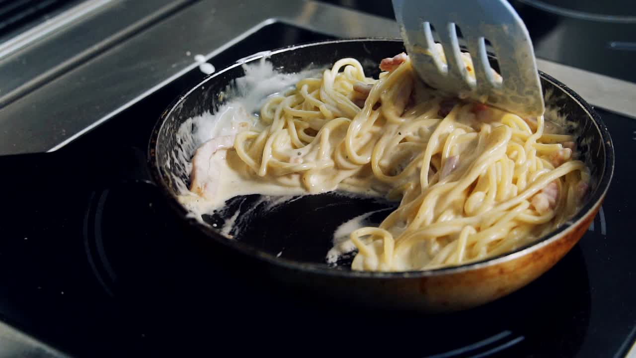 Cooking creamy pasta with bacon. Chef is stirring delicious spaghetti with spatula on a frying pan. Italian cuisine. Close-up