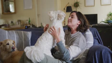 smiling caucasian woman kissing and cuddling her pet dog sitting on sofa at home