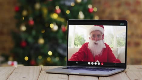 Hombre-Caucásico-Mayor-Disfrazado-De-Santa-En-Videollamada-En-Computadora-Portátil,-Con-Adornos-Navideños-Y-árbol