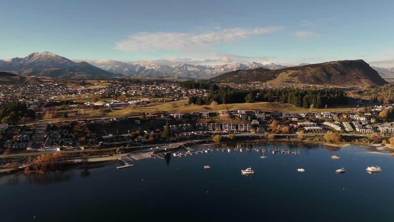 Boats and yachts at port bay of wanaka town during sunset time. Aerial wide shot. Luxury waterfront houses and mountains in background