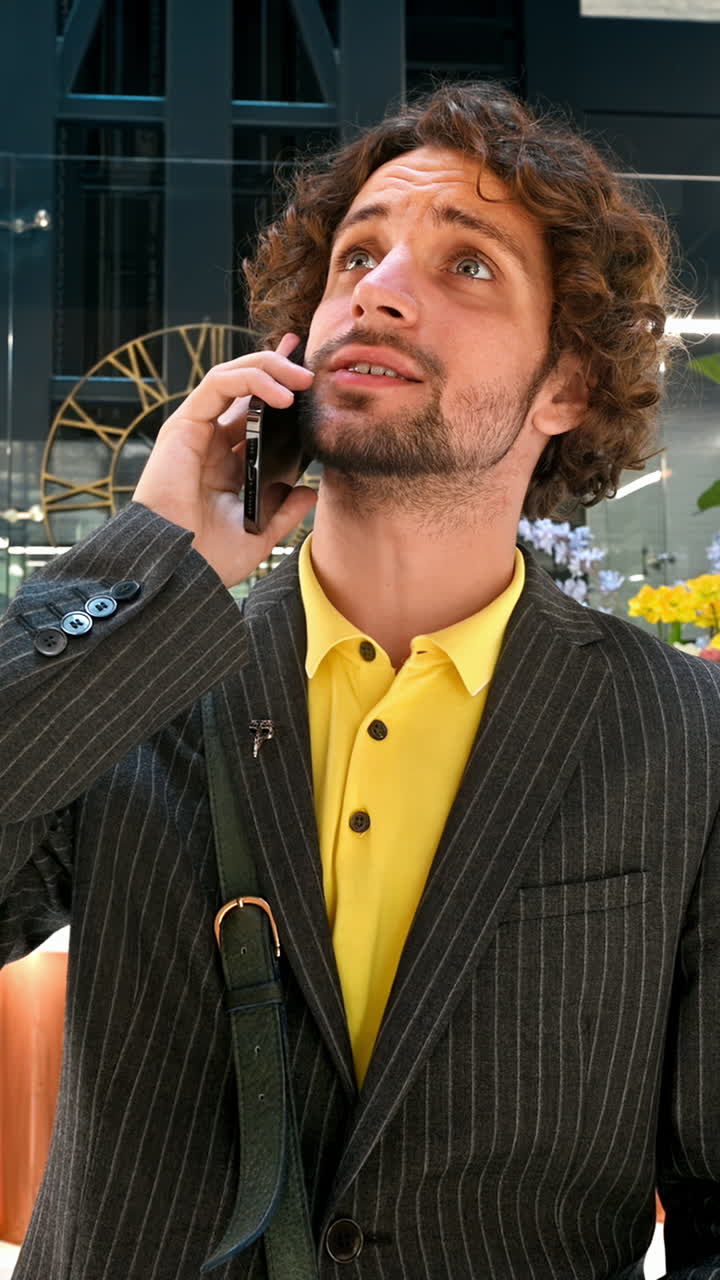 Mann mit gelbem Hemd und grauem Blazer, der in einem Bürogebäude telefoniert. Vertikal