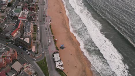 Luftaufnahme-über-Den-Strand-Von-Renaca-Bei-Sonnenuntergang-Mit-Gebäuden-Und-Autos-Im-Hintergrund