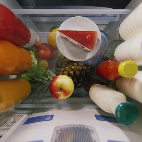 young woman opening fridge door and taking out a piece of cake and a lot of sweets