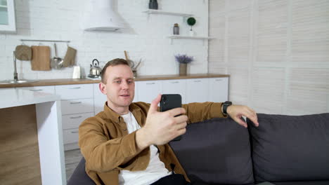 Young man using web camera. Guy doing video call while sitting at home on sofa. Handsome male blogger doing a video chat from his apartment.