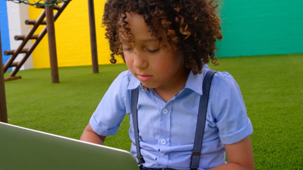 Front view of mixed-race schoolgirl studying on laptop in school playground 4k