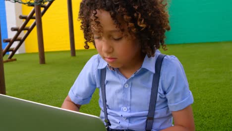 vista frontal de una escolar de raza mixta estudiando en una computadora portátil en el patio de recreo de la escuela 4k