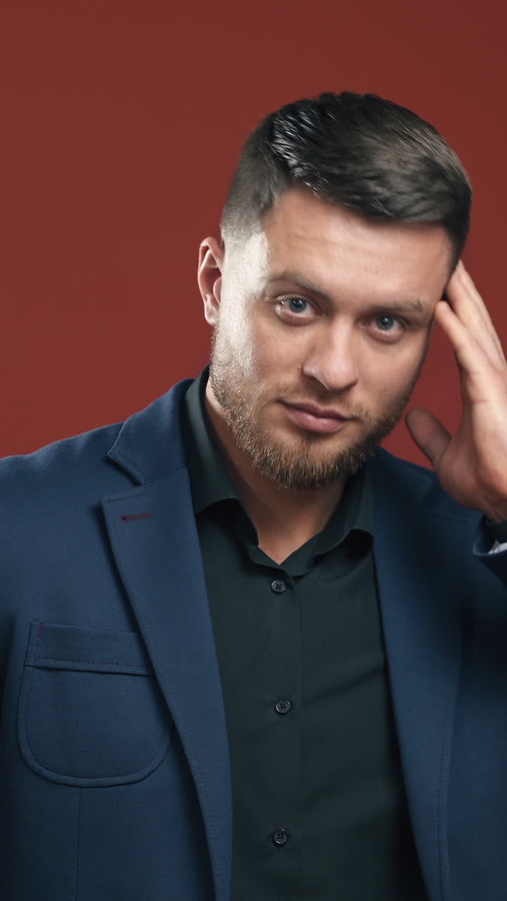 Cheerful young man in suit standing and touching his jacket. Handsome businessman. Dark red backgound. Half waist selective focus. Vertical video