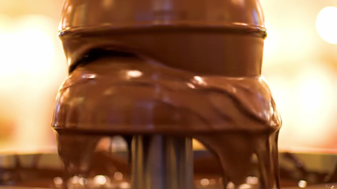 Guests gather around a chocolate fountain at a dessert event. Melted chocolate cascades down, creating a tempting display. People dip various treats into the warm chocolate.