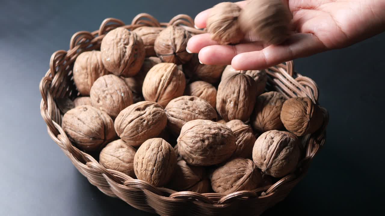 Primo piano di una mano che tiene una noce, con un cesto pieno di noci sullo sfondo