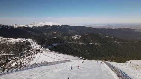 Stabilisierter-Schuss-Eines-Schneebedeckten-Berghangs,-Während-Die-Leute-An-Einem-Sonnigen-Wintertag-Ski-Fahren