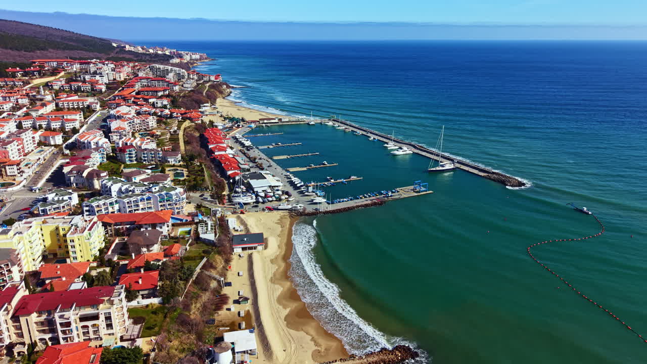 Una veduta costiera di una città con barche ormeggiate nel porto turistico lungo la riva in una giornata di sole.