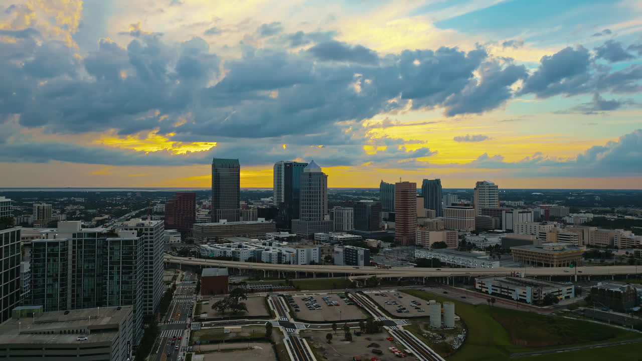 Tampa downtown blocks and skyscrapers with orange glow in sky as the sun is just starting to set, aerial tracking right
