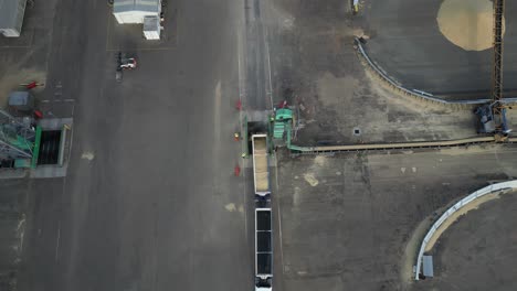 aerial top down shot of grain cargo truck unloading grain into grid, operator opens truck door - industrial distribution process