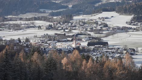 Alpine valley is lightly dusted with the first snow. Villages are scattered along the valley. A red-steepled church stands in the center. Bolzano, Italy.
