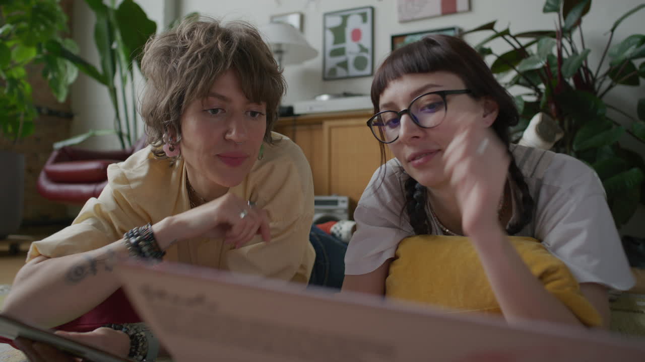 Two Young Women Lying on Floor in Living Room, Discussing Vinyl Albums