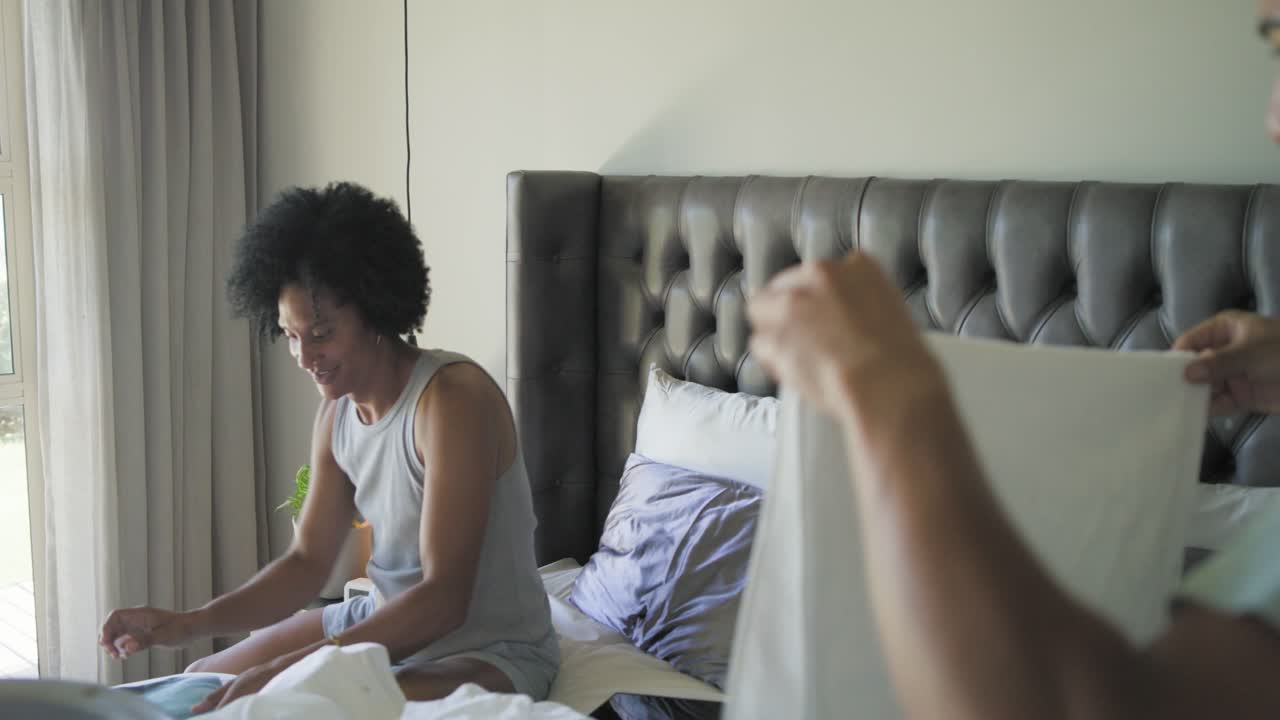 Pai e filho afro-americanos lidando com a cesta de roupa suja, separando e dobrando roupas de cama na cama.