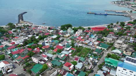 Establishing-Aerial-View-of-lively,-island-town-facing-idyllic-ocean-bay-with-harbours-and-a-lone-rock-water-breaker