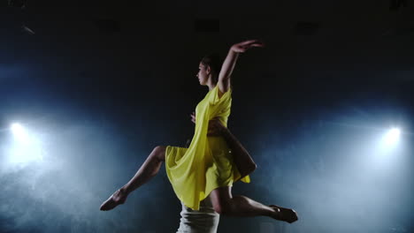 una joven con un vestido blanco baila contemporáneamente en cámara lenta en el escenario con humo en los reflectores. la cámara se mueve alrededor de la bailarina.