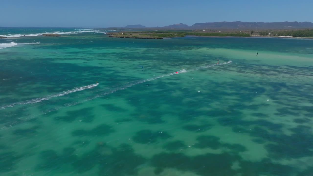 Aerial view as the drone follows kitesurfers racing through clear turquoise waters in Sakalava Bay