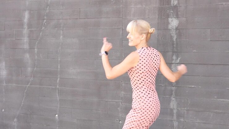 A woman dancing in a pink polka dot dress by a gray brick wall with a carefree attitude outdoors