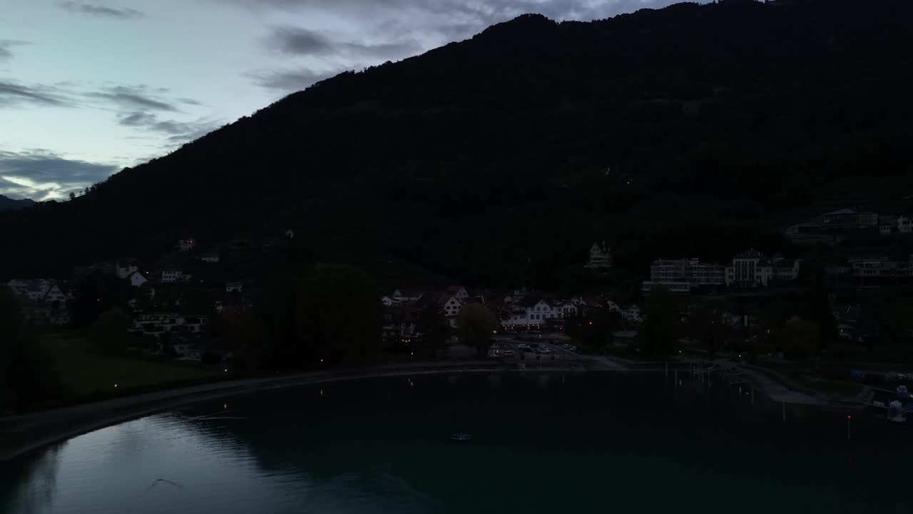 Aerial view of a residential coastal area along Lake Walensee in Switzerland during the late evening, with dusk setting in, highlighting charming homes nestled against the tranquil waters.