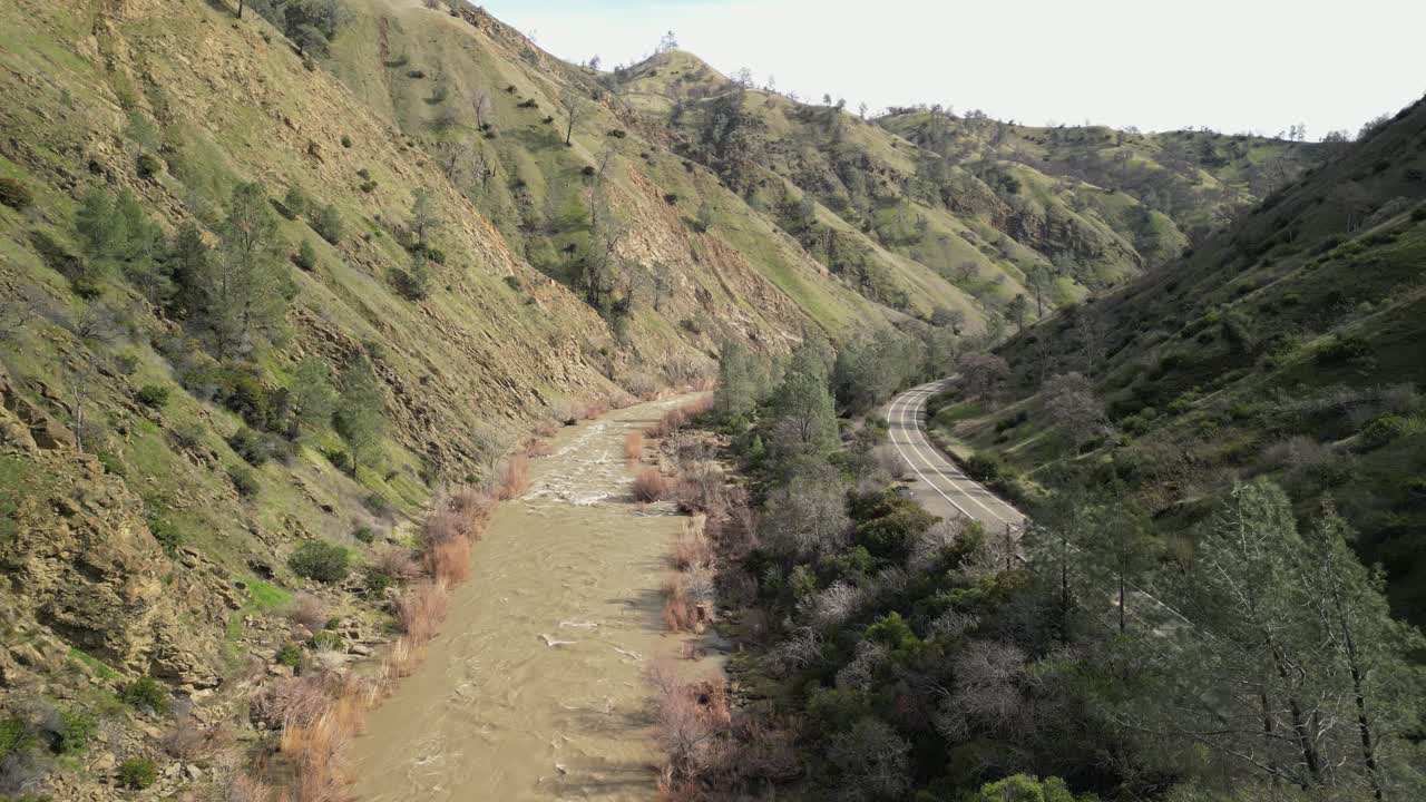 Golden hills and lush trees frame the flowing waters of Cache Creek in this overhead drone perspective.