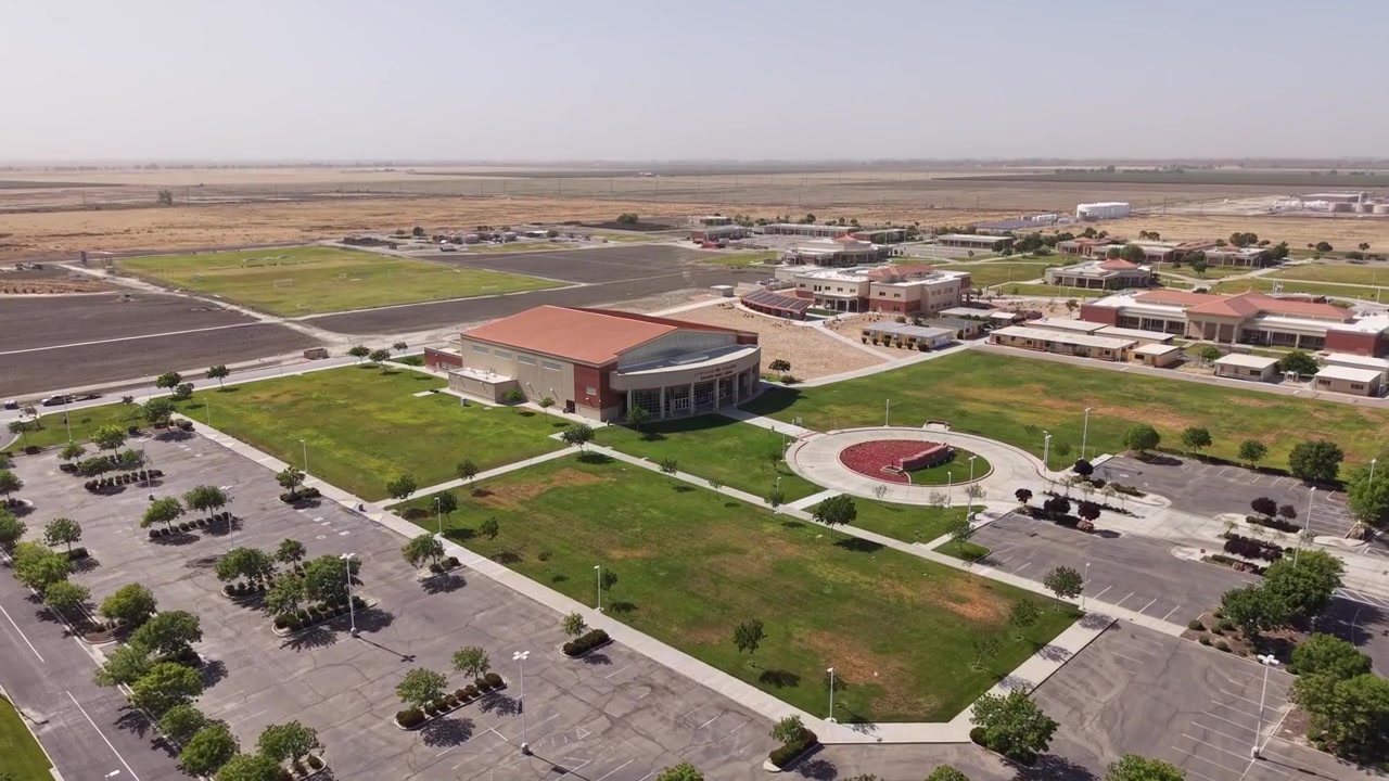 Rising drone view showing the campus and parking lot of Lemoore College in Lemoore, California, surrounded by the agricultural fields of the San Joaquin Valley on a clear day