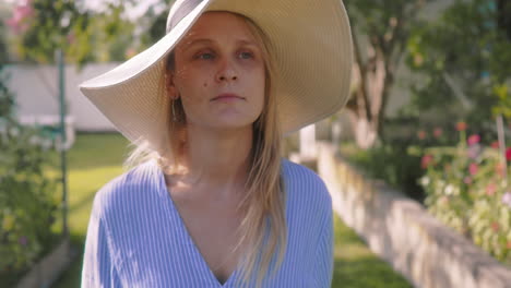 a young woman in a straw hat smiles as she looks away in a garden.