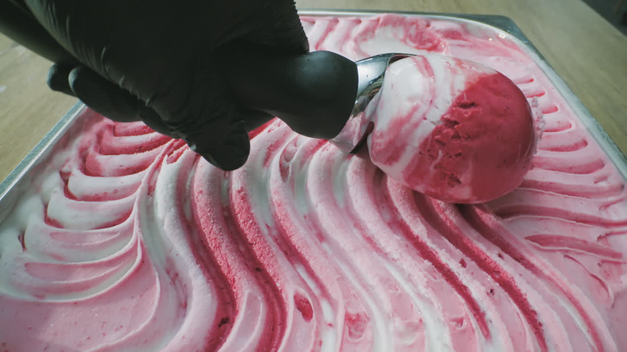 A close-up of a creamy, tempting, two-tone ice cream being scooped out with a metal scoop. Its smooth texture, vibrant colors, and captivating movement are captured in high definition.