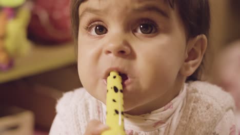 a cute baby biting a yellow toy before throwing it - close up