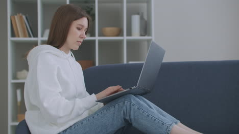 woman using laptop on couch at home. thoughtful young woman sitting with computer on couch looking outside concentrate on work feeling bored need additional motivation working remotely at home.