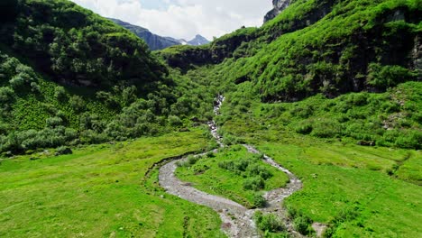 Aerial-flyover-of-meltwater-stream,-backward-dolly-revealing-majestic-Swiss-alps