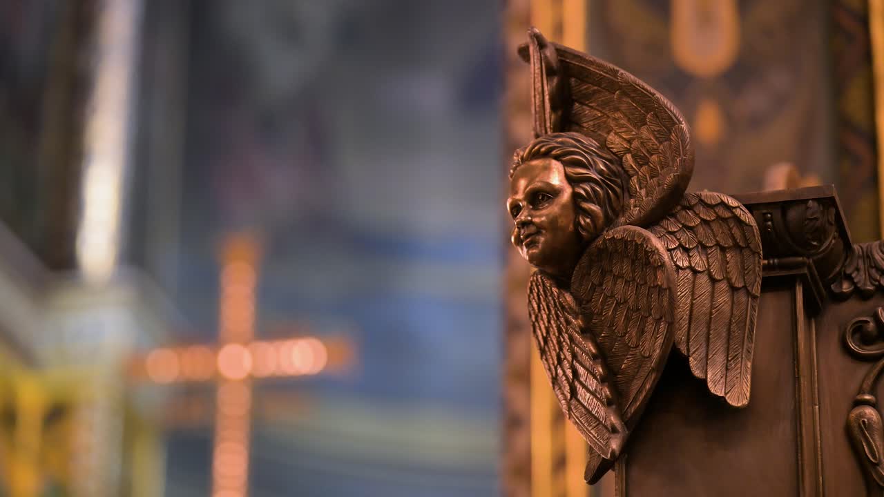 The intricate craftsmanship of sacred art inside St. Volodymyr's Cathedral in Kyiv, Ukraine. This close-up reveals a detailed angel sculpture with an illuminated cross blurred in the background.