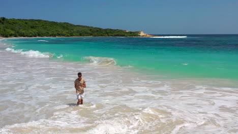 Chico-Parado-En-El-Mar-Volando-Un-Dron,-Playa-De-Half-Moon-Bay,-Antigua,-Caribe