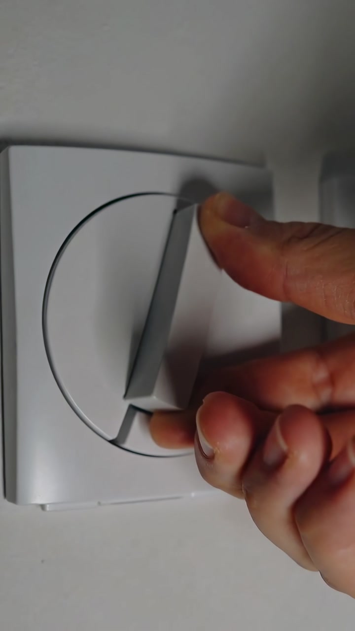 Vertical video: Grasping right hand adjusting white circular dimmer at living room, dimming lights