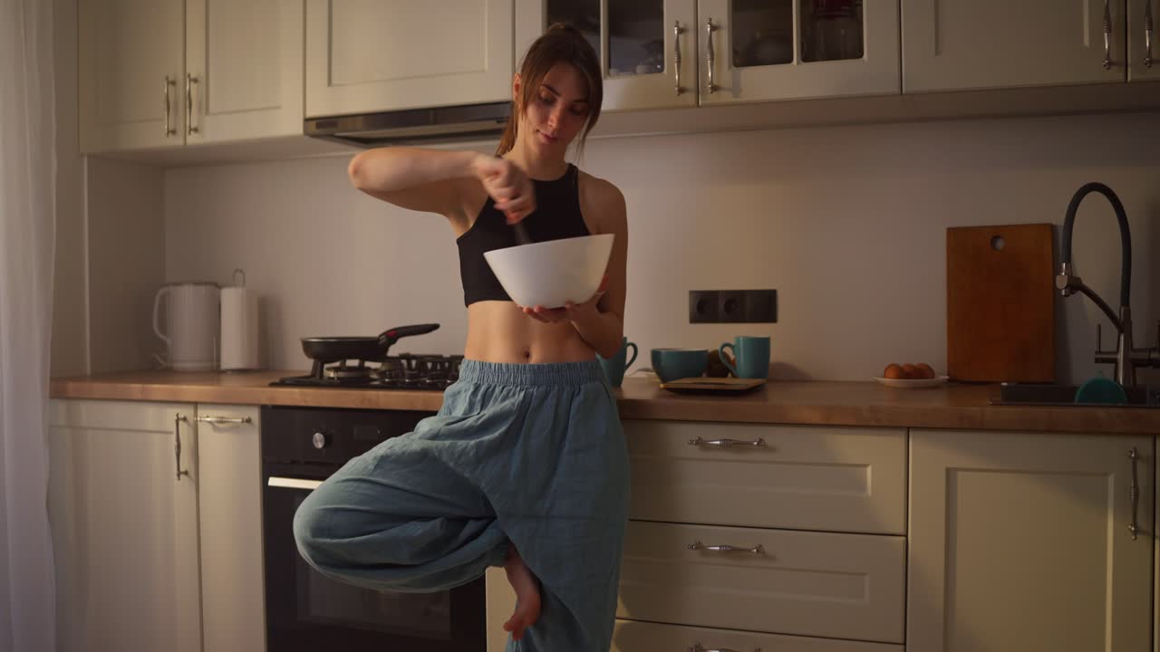 Donna che prepara cibo in cucina mentre fa yoga