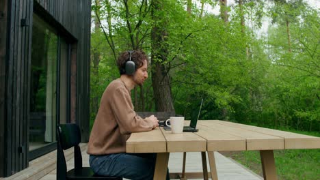 man working remotely from a wooden table in a forest setting.