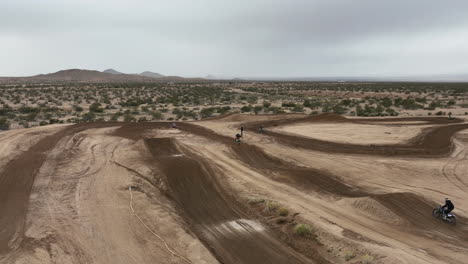motociclistas corriendo en una pista todoterreno y haciendo largos saltos desde rampas de tierra en cámara lenta - vista aérea