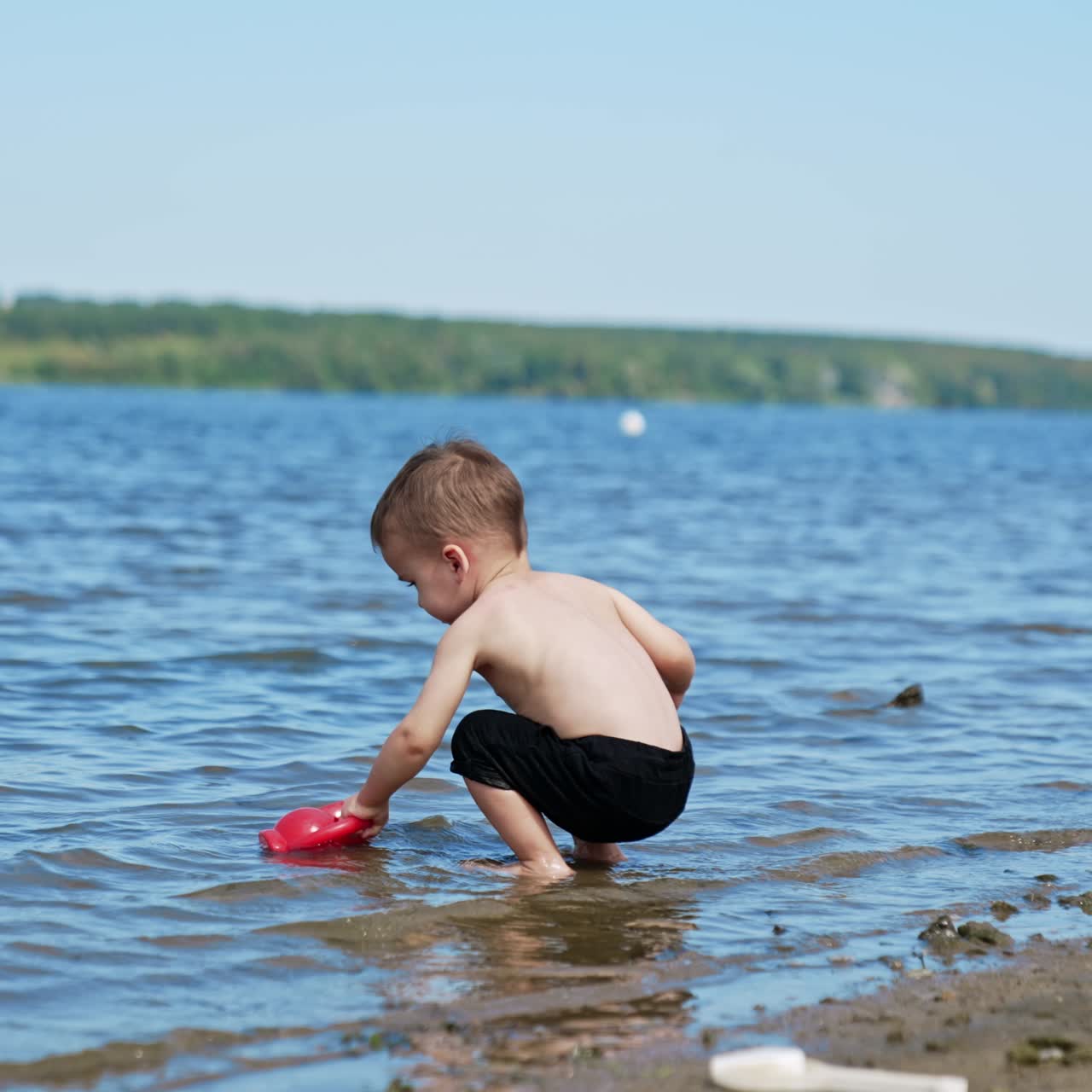 Un bebé adorable pasa tiempo en la playa en verano. Un niño pequeño se mete en el agua para llenar su regadera.