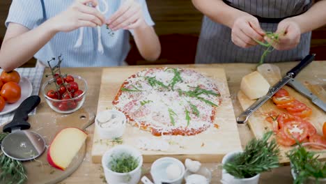 still shot of two cooks setting toppings on a homemade pizza placed on a wooden cutting board