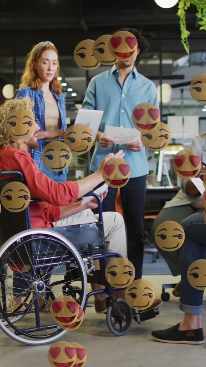 Vídeo vertical: Homem em cadeira de rodas apontando, equipe observando enquanto uma chuva de emojis surge e depois desaparece em reunião.
