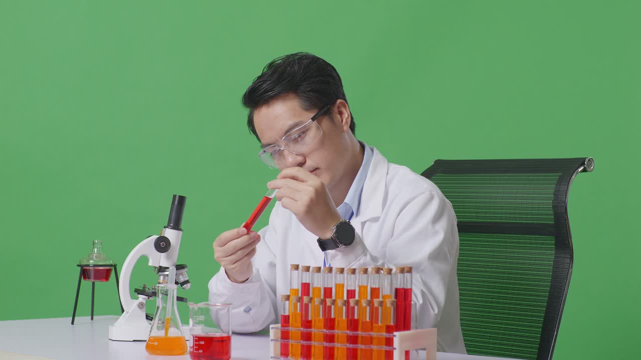 Side View Of Asian Man Scientist Looking At The Red Liquid In The Test Tube And Shaking Head On The Table With Microscope In The Green Screen Background Laboratory