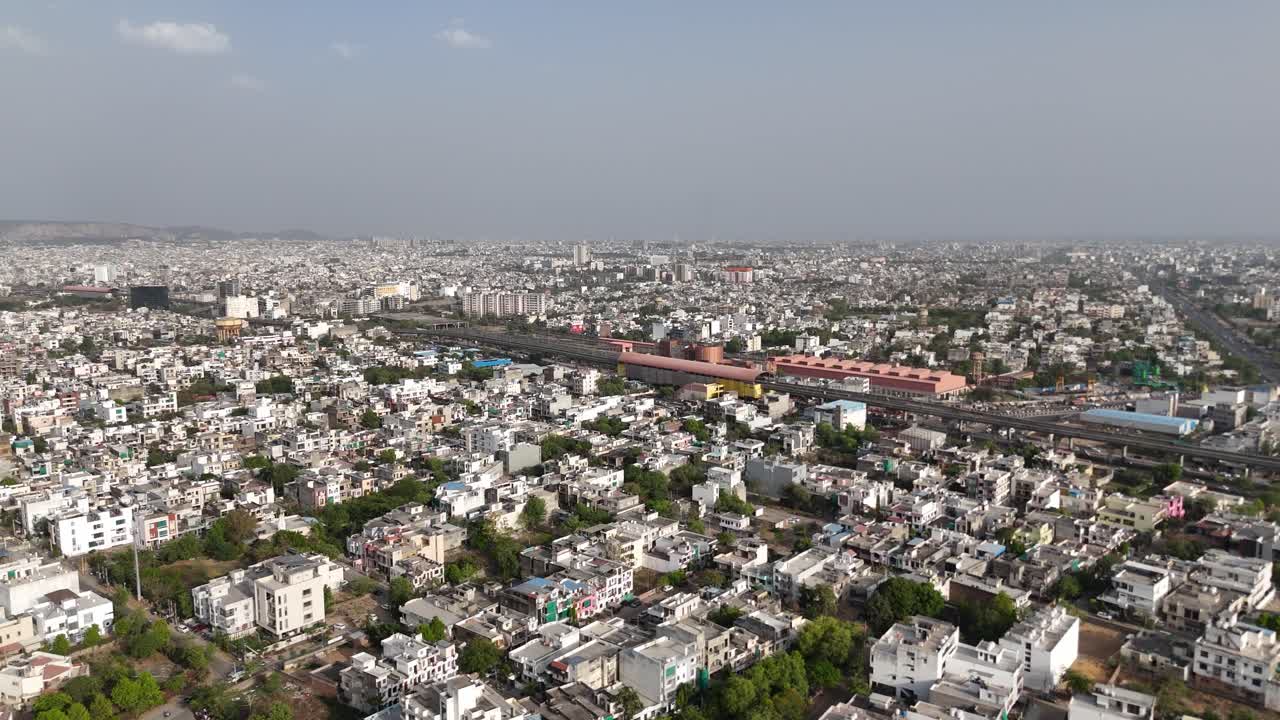 Flyover footage showing high-rise apartments beside older, low-rise colonies and railway track passing through the city