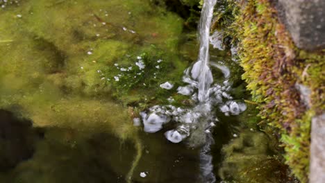 Wasserstrahl,-Der-In-Eine-Bemooste-Wasseroberfläche-Fällt,-Erscheinen-Blasen