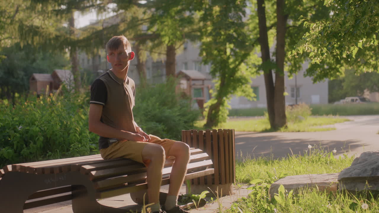 White Man Sitting On Bench Scanning Surroundings With Uneasy Glances, Daylight Park Scene With Trees And Path, Vigilant Posture And Wary Expressions Suggestive Of Social Anxiety And Hypervigilance